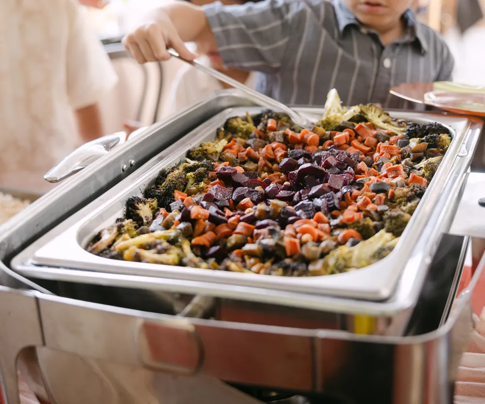 A young guest serving himself roasted vegetables from the buffet