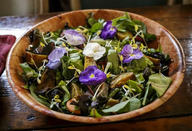 A wooden bowl of salad topped with edible flowers