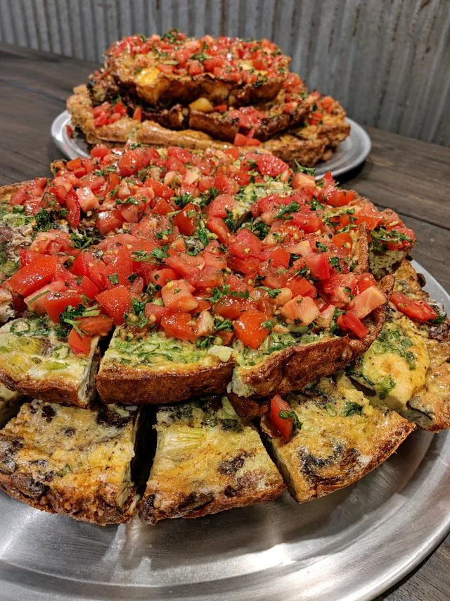 A tortilla espanola topped with fresh tomato and herbs