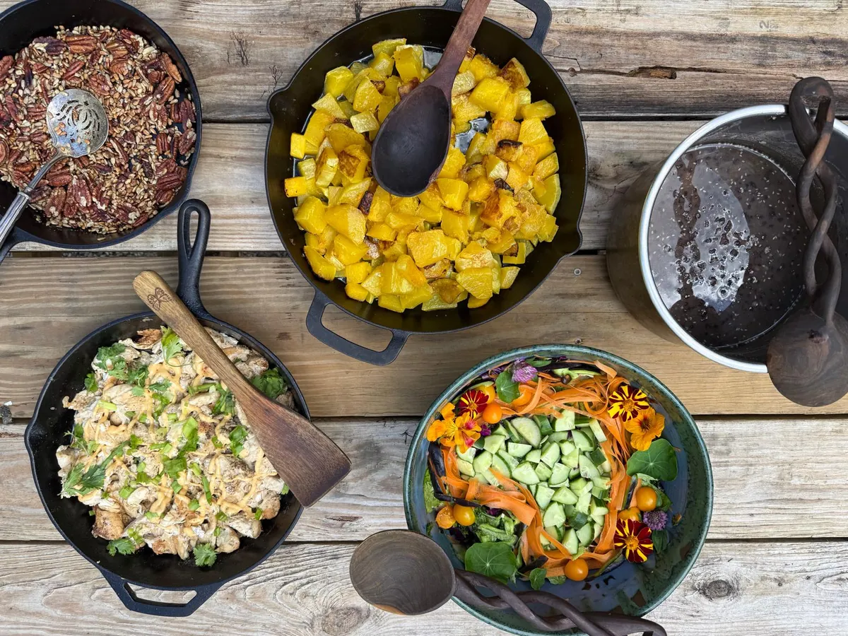 Cast iron skillets of salad, grains, roasted squash and pecans set out for a table to share