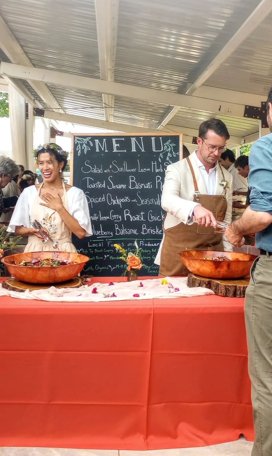 A couple serving their guests from copper bowls beneath a chalkboard menu